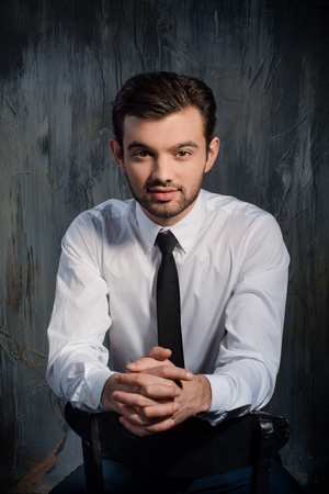 Handsome stylish man sitting on a chair on a gray backgroundの写真素材