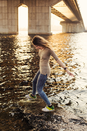 Happy young woman running back from the river waves near bridge in the cityの写真素材