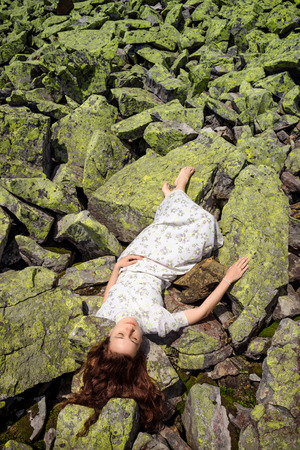 Beautiful young woman lying on stones in white dress whith closed eyesの写真素材