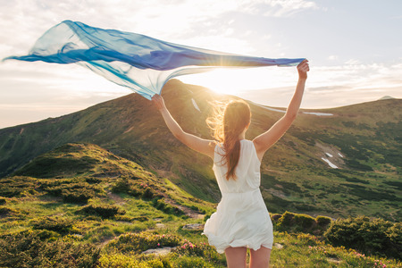 Woman feel freedom standing on the mountain trail through blooming rhododendron valley with blue...