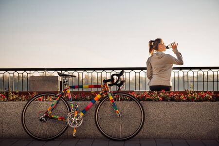 Young woman drinking water after riding a bicycle in the morning cityの写真素材
