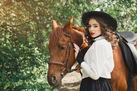 Woman standing with horse near forest and touching to horse faceの写真素材