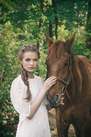 Woman standing with horse near forest and touching to horse faceの写真素材