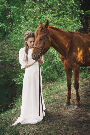 Woman standing with horse near forest and touching to horse faceの写真素材