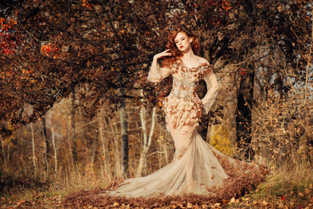 Beautiful elegant woman standing in the autumn forest in chiffon dress with yellow autumn leavesの写真素材