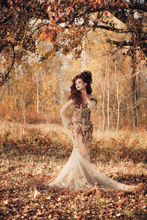 Beautiful elegant woman standing in the autumn forest in chiffon dress with yellow autumn leavesの写真素材