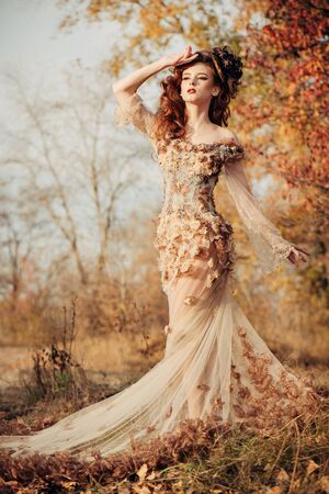 Beautiful elegant woman standing in the autumn park in chiffon dress with yellow autumn leavesの写真素材