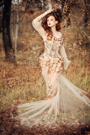 Beautiful elegant woman standing in the autumn park in chiffon dress with yellow autumn leavesの写真素材