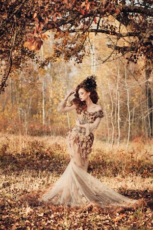 Beautiful elegant woman standing in the autumn forest in chiffon dress with yellow autumn leavesの写真素材