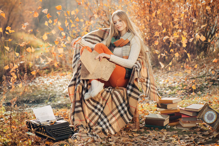 Dreamy woman sitting in the autumn park and writes with fall leaves on backgroundの写真素材