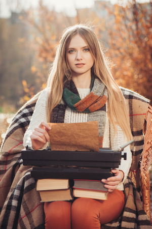 Thinking woman sitting in the autumn park and writes on the old typewriter at sunsetの写真素材