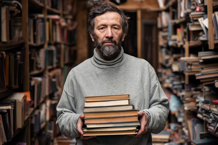 Portrait of authentic senior man with beard and good eyes holding books in the hand on book market backgroundの写真素材