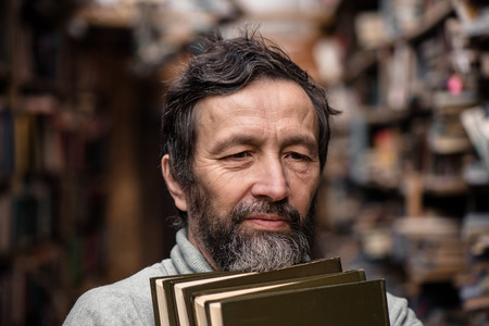Portrait of authentic senior man with beard and good eyes holding books in the hand on book market backgroundの写真素材