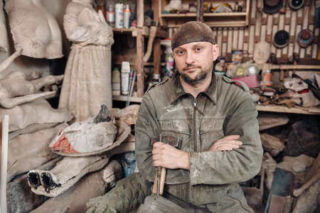 Portrait of sculpture man holding working tools in the hands and sitting in his workshopの写真素材