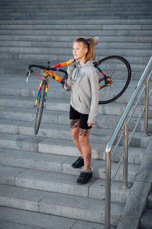 Young woman holding bicycle in the hand and going down the stairs at sunriseの写真素材