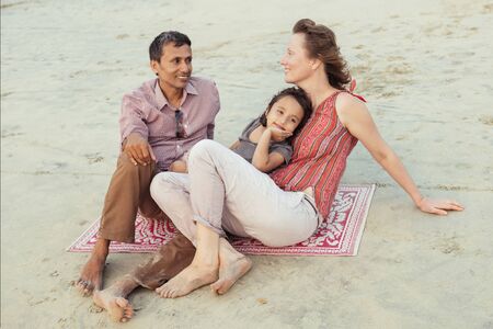 Happy mixed race family having fun on the beach at sunsetの写真素材