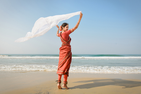 Indian woman feel freedom and standing near the beach in traditional saree clothing with white tissue in the handsの写真素材