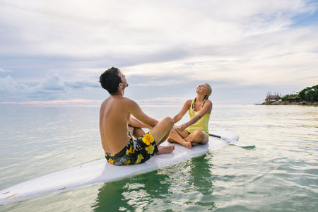 Young couple sitting on the paddle board near the beach and enjoying sunsetの写真素材