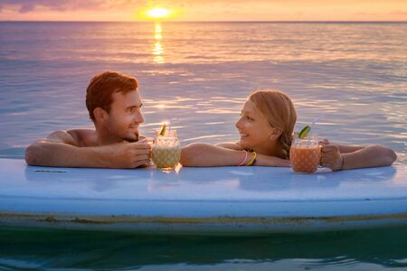 Young couple swiming with paddle board in the sea  at sunset and drinking fruit cocktailsの写真素材