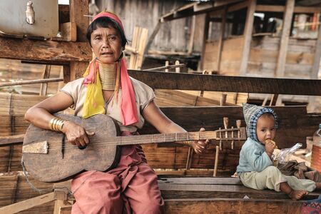 Pan Pet, Myanmar - May 25, 2016: Padaung (Karen) woman sitting with child and playing guitar near the house, Myanmarのeditorial素材