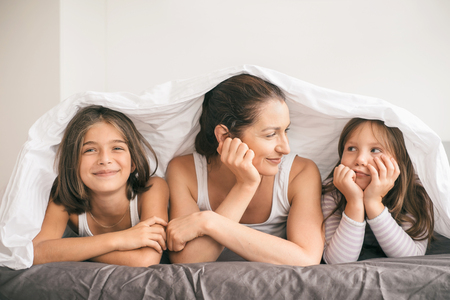 Mother with children have fun and lying in the bed covered with blanketの写真素材