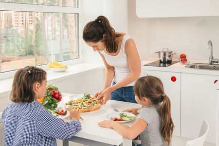 Beautiful young mother preparing for her little daughters delicious vegetable pie. Concept healthy lifestyle in modern familyの写真素材