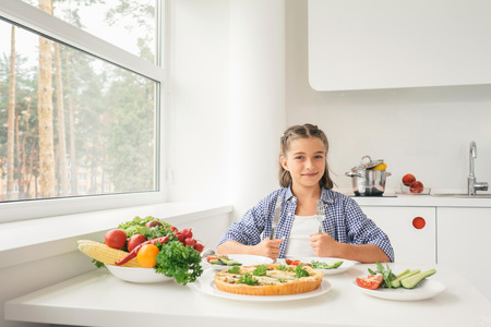 Hungry little girl sitting by table in the kitchen and ready to have meal. Concept healthy lifestyle in modern familyの写真素材