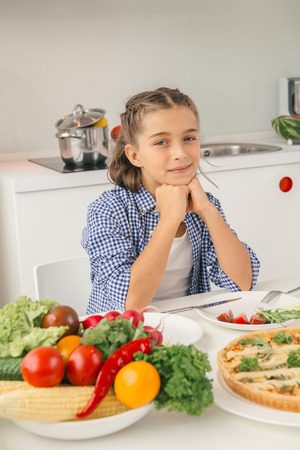 Cute little girl sitting by table in the kitchen and ready to have meal. Concept healthy lifestyle in modern familyの写真素材