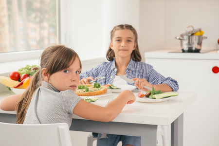 Hungry little girl sitting by table in the kitchen and ready to have meal. Concept healthy lifestyle in modern familyの写真素材