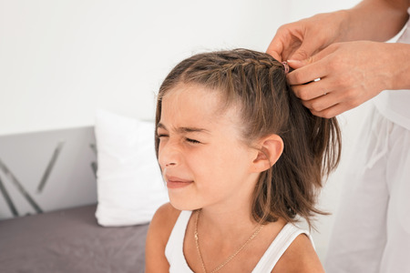 Mother making braids to her daughter at home in the bedroomの写真素材