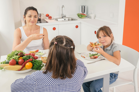 Young mother and daughters eating healthy food in kitchen. Concept healthy lifestyle in modern familyの写真素材