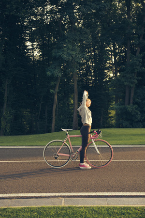 Young woman on bike standing on road and doing stretching exercise. Active lifestyle.の写真素材