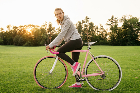 Active  young woman on bike standing on road and looking to somewhereの写真素材