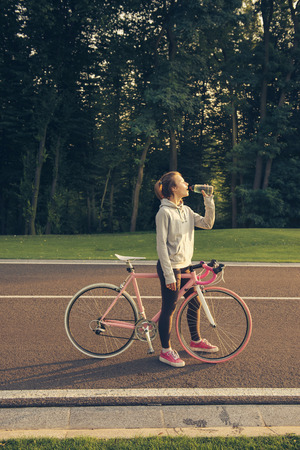 Young woman on bike standing on road and doing stretching exercise. Active lifestyle.の写真素材