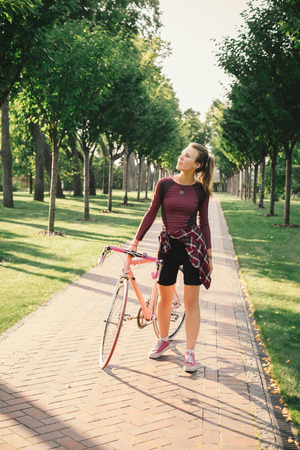 Active young woman on bike standing on road and looking to somewhereの写真素材