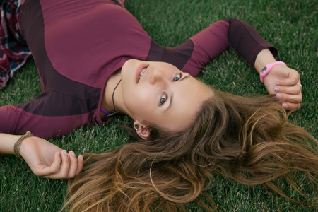 Young athlete woman resting and relaxing after fitness exercise. Woman lying on the green grass in city park.の写真素材