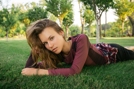 Young athlete woman resting and relaxing after fitness exercise. Woman lying on the green grass in city park.の写真素材