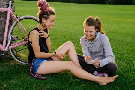 Two hipster woman with bicycle in city park having fun together. Outdoor shot of happy young female friendsの写真素材