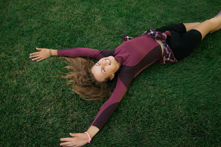 Young athlete woman relaxing after fitness exercise. Woman lying on the green grass and stretching her armsの写真素材