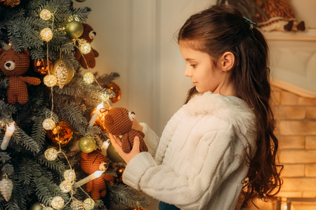 Happy child decorating Christmas tree with toys in the evening. Winter weekends. Cozy scene. Holiday atmosphere.の写真素材