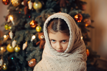 Sad little girl covered in warm scarf and waiting for  gift in Christmas eveの写真素材