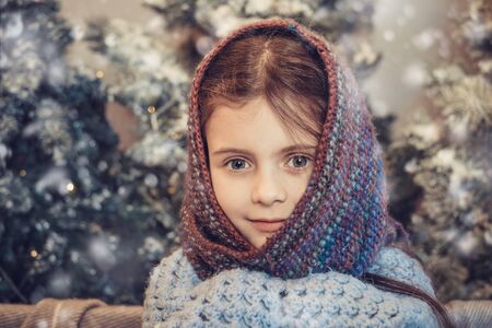Portrait of cute little girl covered in warm scarf near cozy christmas decoration. Child waiting for gift in Christmas eveの写真素材