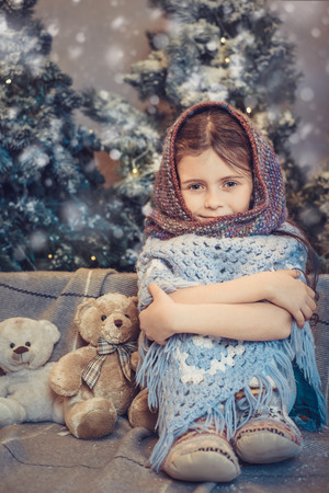Portrait of cute little girl covered in warm scarf near cozy christmas decoration. Child waiting for gift in Christmas eve. Holiday atmosphere.の写真素材