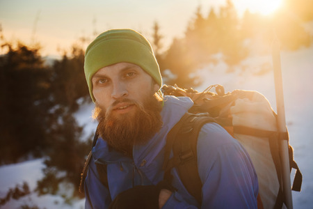 Portrait of bearded hipster man with climbing equipment in winter mountain at sunset