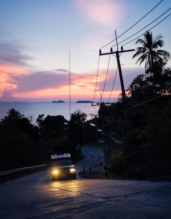 Beautiful mountain road with car in night time over the sea at sunset background. Travel to Phangan island in Thailand.の写真素材