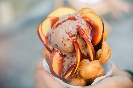 Tasty ice cream in hands with bubble waffle cone and fruits on blurred backgroundの写真素材