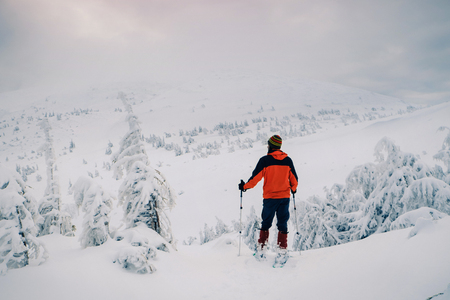 Man hiker stand with trekking sticks on the mountain summit over the clouds and enjoying beautiful winter landscape. Winter sport activityの写真素材