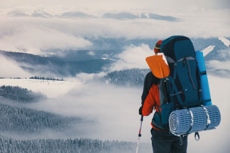 Man hiker stand with trekking sticks on the mountain summit over the clouds and enjoying beautiful winter landscape. Winter sport activityの写真素材