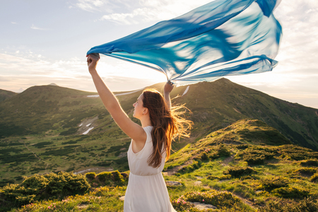 Woman feel freedom and enjoying the nature in the mountains with blue tissue in hands on sunsetの写真素材