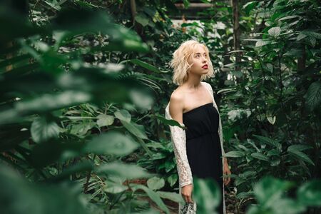 Beautiful young fashion woman with blond hair and perfect figure posing in the palm leaves in the jungle. Young pretty girl in green tropical forest or greenhouseの写真素材